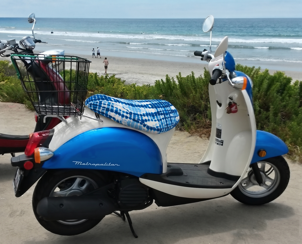 Shibori Tide seat cover fitted to a blue-and-white Honda Metropolitan beside the beach, handmade by Cheeky Seats.