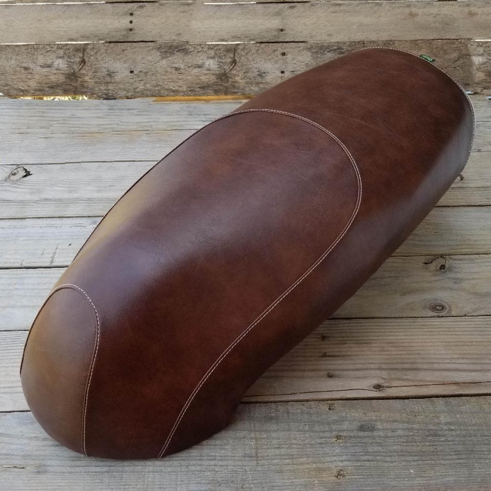 Overhead angle on a weathered wood deck showing the whiskey brown distressed leather-look Kymco Like seat cover with tan contrast stitching, handmade by Cheeky Seats
