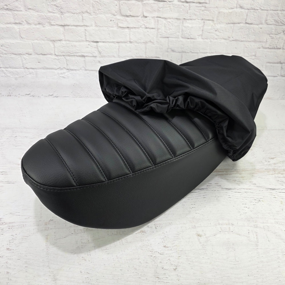 Black elasticated rain and dust cover being fitted over a Honda DAX 125 seat, from Cheeky Seats