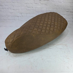 Brown quilted seat cover on a white surface with a light gray brick wall background