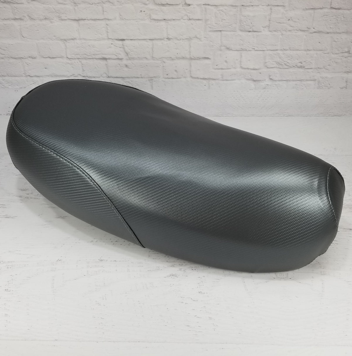 Three-quarter view of a gray carbon-fiber-textured Yamaha Zuma II BWS 49/50 Prebug seat cover, handmade by Cheeky Seats
