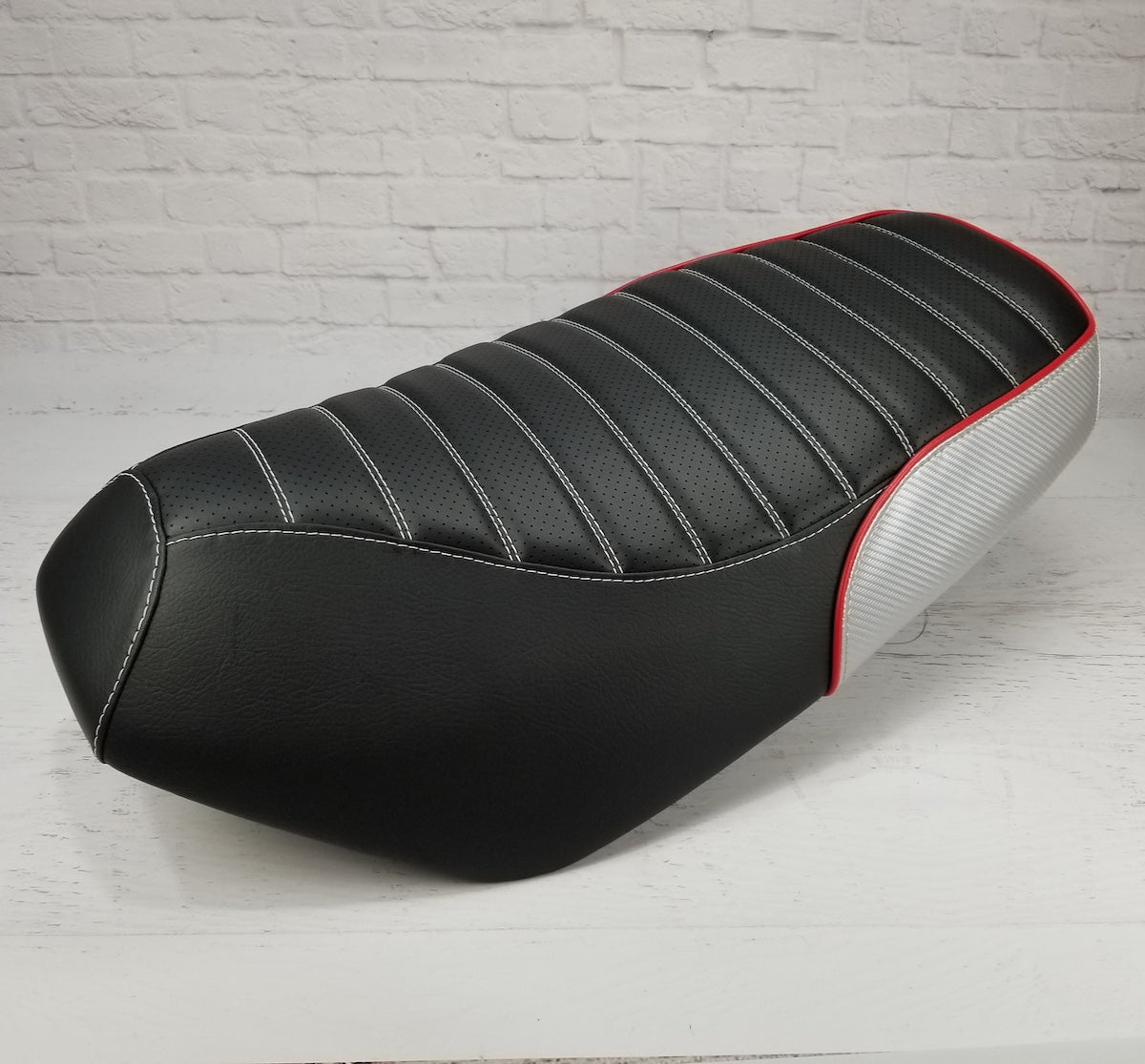 Side profile of the Yamaha Zuma 50 tuck-and-roll seat cover showing padded channels and contrasting rear trim, handmade by Cheeky Seats.